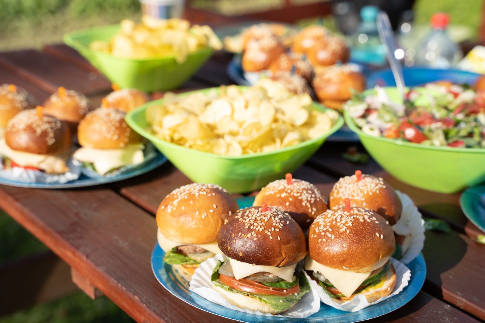 Buffet table with many mini burgers at outdoors birthday party for children, kids. Catering at wedding day. Bright tasty hamburgers with fish, chicken, meat, salad. Dinner in country house in village.